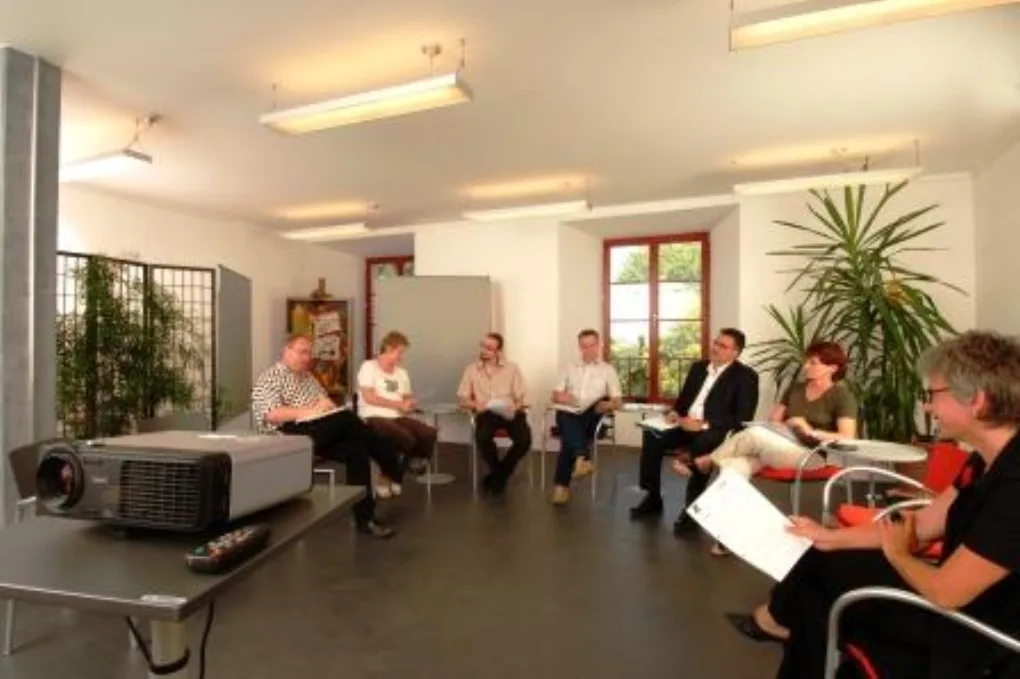 Organisationsentwicklung im Stuhlkreis: eine Gruppe diskutiert in einem Seminarraum, im Vordergrund ein Beamer.